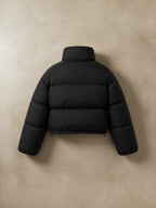 Chaqueta puffer cropped negra cozyvibe con cuello alto y diseño acolchado, vista trasera sobre fondo neutro.