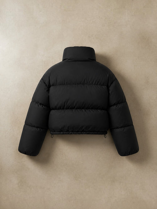 Chaqueta puffer cropped negra cozyvibe con cuello alto y diseño acolchado, vista trasera sobre fondo neutro.