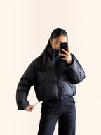 Chaqueta puffer cropped negra cozyvibe con cuello alto, cierre frontal y cordón ajustable en la cintura