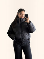 Modelo vistiendo chaqueta puffer cropped negra cozyvibe con cuello alto y ajuste en cintura, estilo invernal moderno