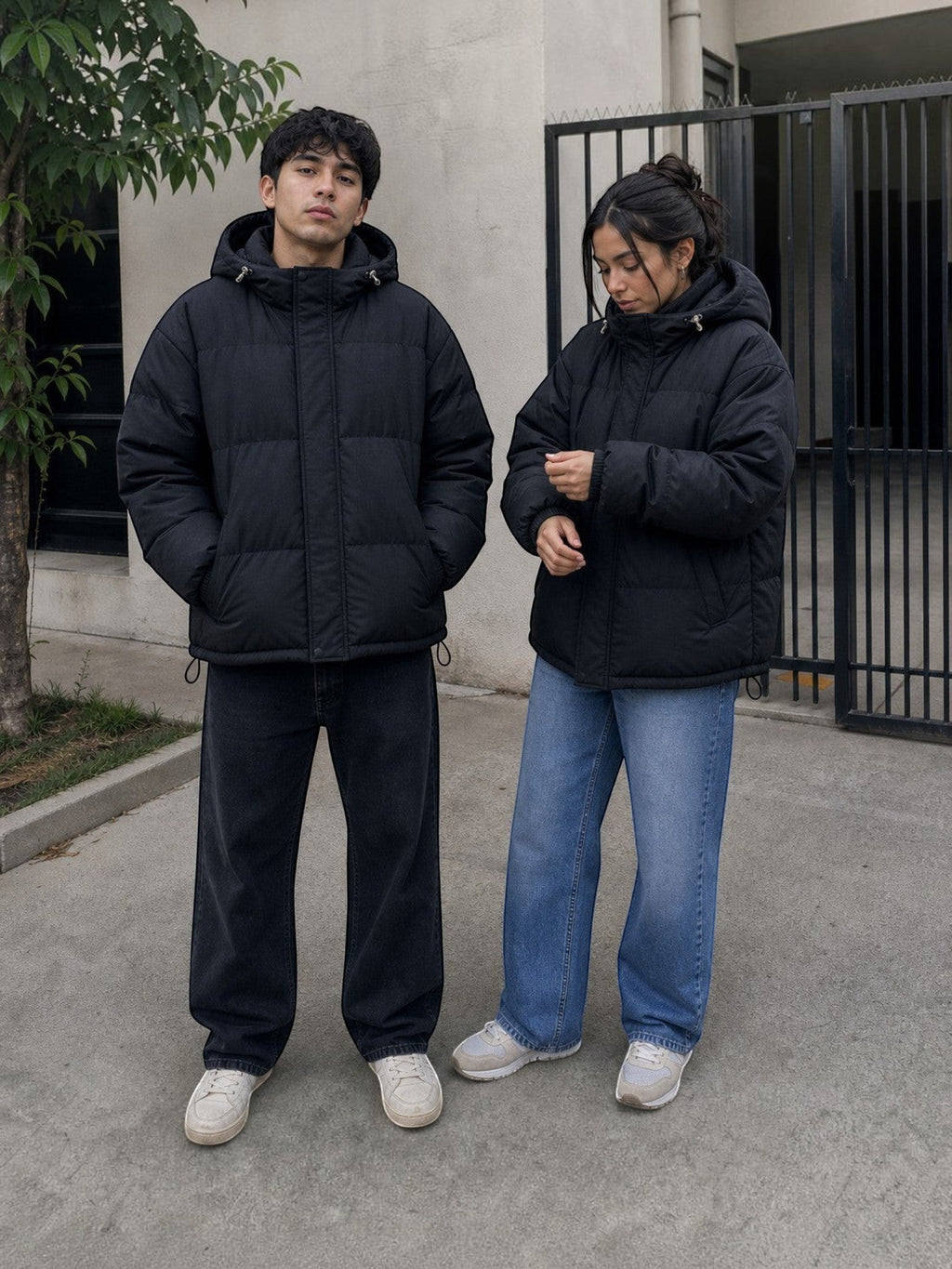 Chaqueta puffer negra oversize unisex de cozyvibe con capucha y cierre frontal, usada por un hombre y una mujer