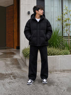 Chaqueta puffer negra oversize unisex de cozyvibe con capucha y cierre frontal, usada por un joven en exterior