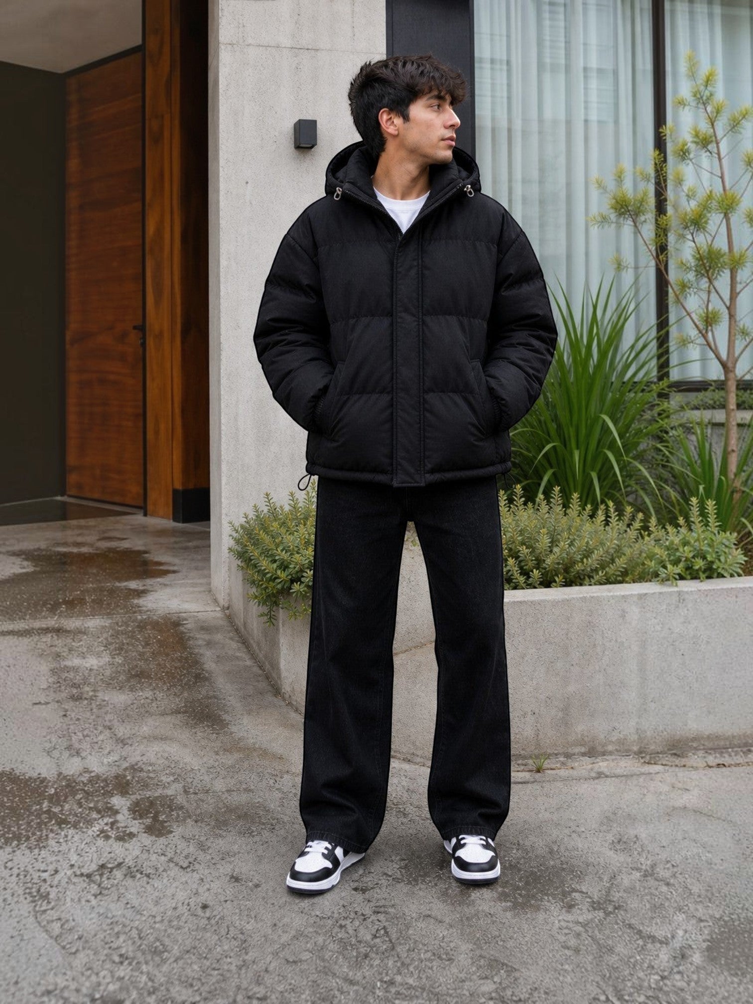 Chaqueta puffer negra oversize unisex de cozyvibe con capucha y cierre frontal, usada por un joven en exterior