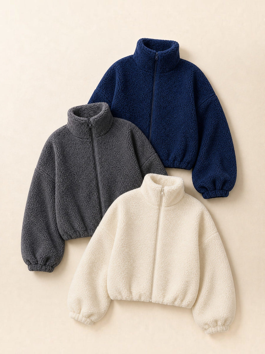 Tres polerones cozyvibe de chiporro teddy con cuello alto y cierre frontal en colores azul, gris y albaricoque.